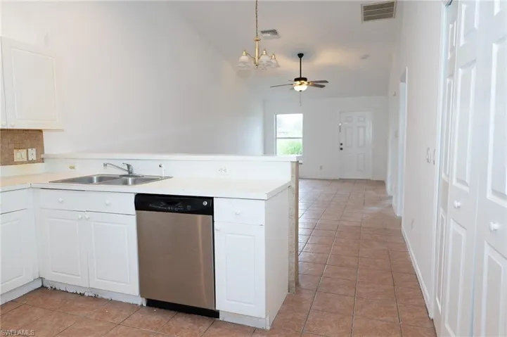 Kitchen featuring white cabinets, light countertops, stainless steel dishwasher, pendant lighting, and a peninsula