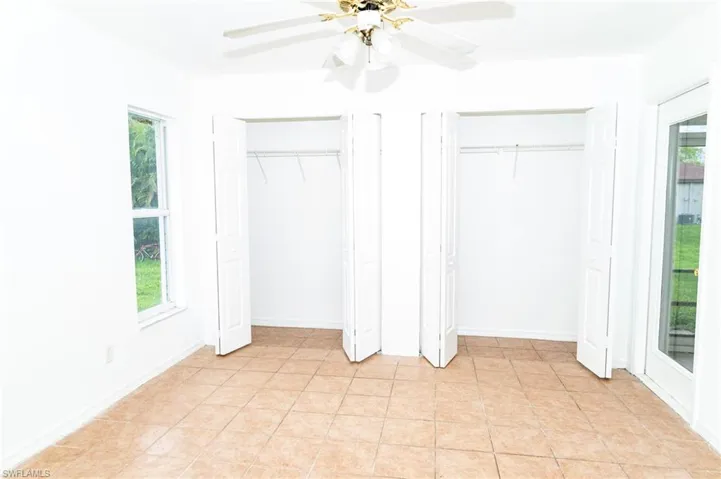 Unfurnished bedroom with two closets, light tile patterned floors, and ceiling fan