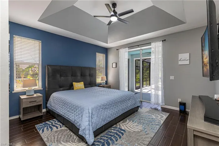 Bedroom featuring wood tiled floors, a tray ceiling, access to outside, multiple windows, and ceiling fan