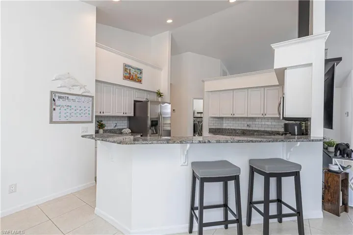 Kitchen with a breakfast bar, backsplash, dark stone countertops, and vaulted ceiling