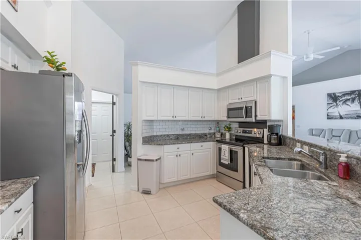 Kitchen featuring stainless steel appliances, dark stone counters, white cabinetry, and lofted ceiling