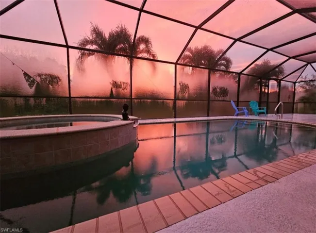 Pool at dusk featuring a pool with connected hot tub, a sunroom, and glass enclosure