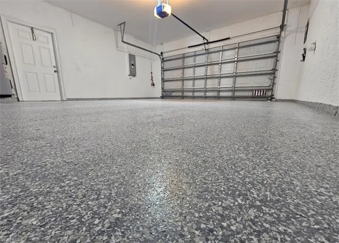 Garage with a textured wall, a garage door opener, and electric panel