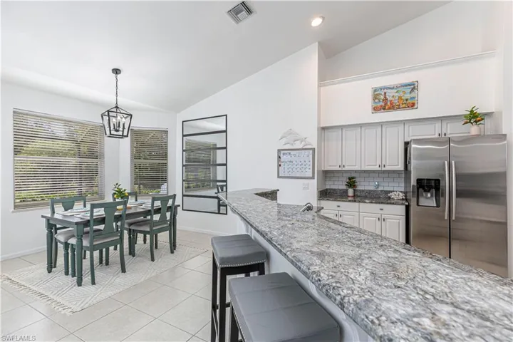 Kitchen with lofted ceiling, a kitchen breakfast bar, stainless steel refrigerator with ice dispenser, dark stone countertops, and light tile patterned floors