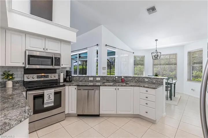 Kitchen with stainless steel appliances, white cabinets, a peninsula, backsplash, and light tile patterned floors