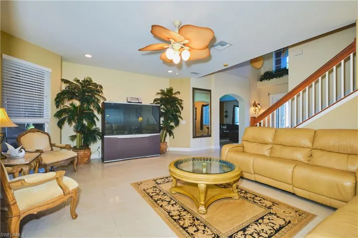 Living room with light tile patterned floors, arched walkways, ceiling fan, and recessed lighting