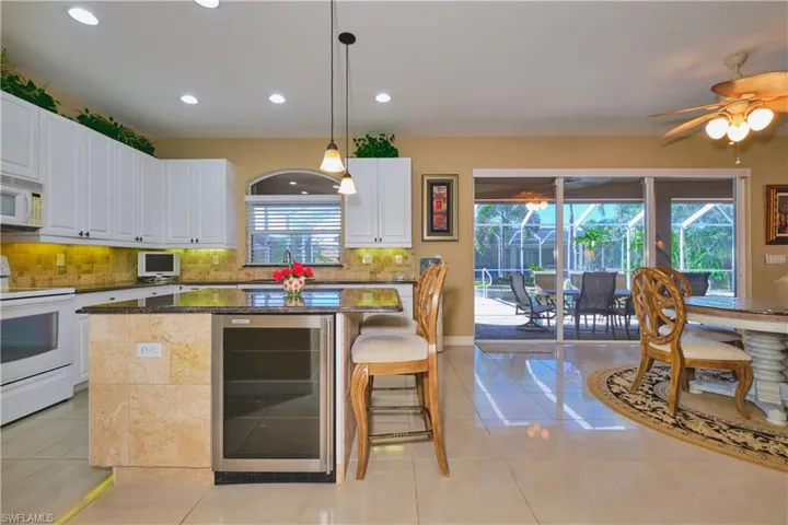 Kitchen featuring wine cooler, white appliances, pendant lighting, tasteful backsplash, and a kitchen breakfast bar
