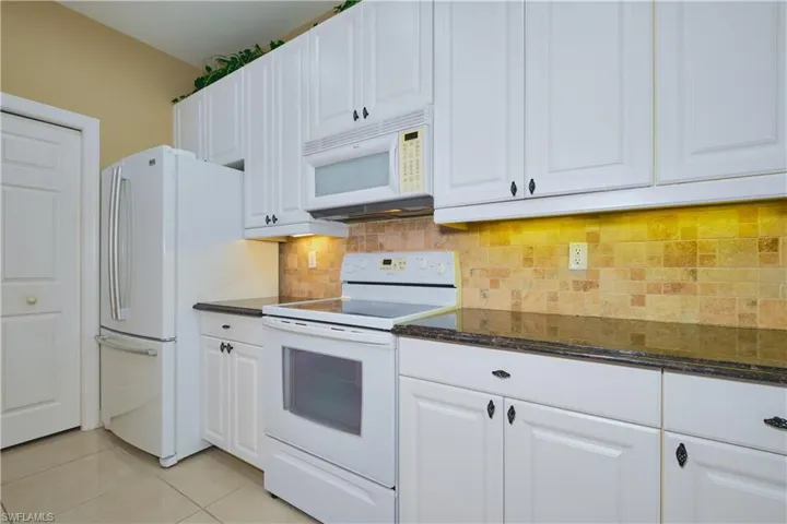Kitchen with white appliances, white cabinets, tasteful backsplash, and dark stone countertops