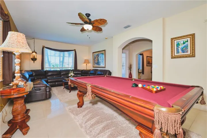 Recreation room featuring arched walkways, light tile patterned floors, billiards, and a ceiling fan