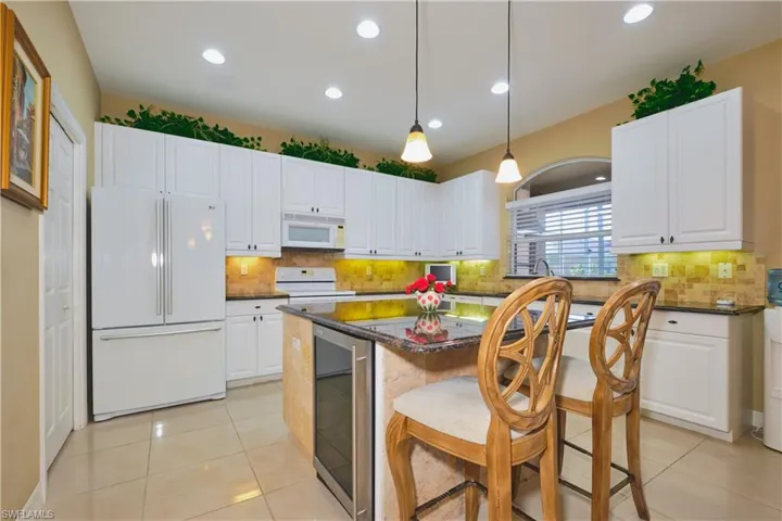 Kitchen featuring white appliances, decorative light fixtures, beverage cooler, a kitchen breakfast bar, and dark stone countertops