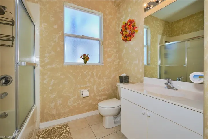 Full bath with bath / shower combo with glass door, vanity, light tile patterned flooring, and wallpapered walls