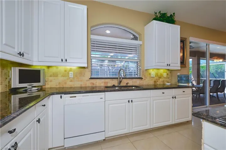 Kitchen with dark stone countertops, white cabinetry, dishwasher, light tile patterned floors, and backsplash