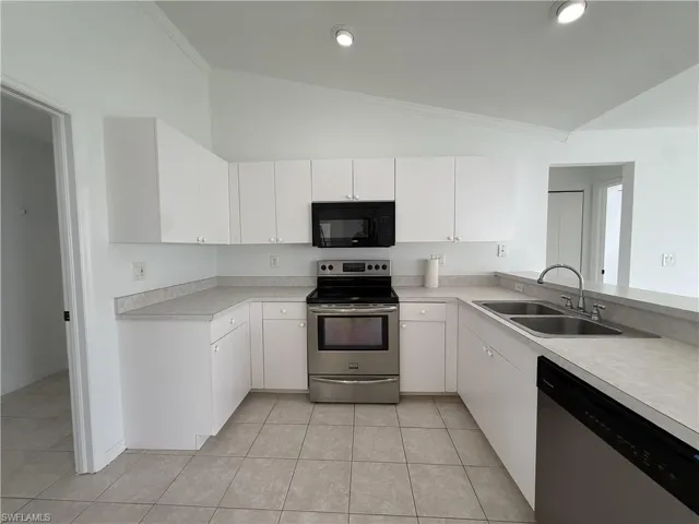 U-shaped kitchen featuring white cabinetry, gray countertops, stainless steel appliances, a dual basin sink with a high-arc faucet, and tiled flooring