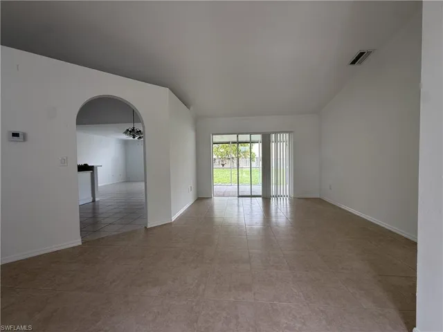 Spacious living area featuring neutral ceramic tile flooring, vaulted ceilings, and a sliding glass door providing access to the outdoor area
