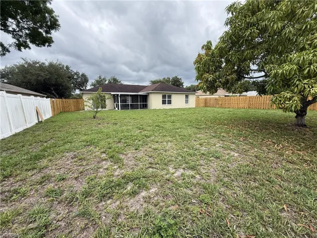 Spacious backyard featuring a screened-in patio, partial privacy fencing, and mature trees