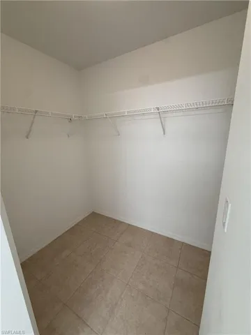 Walk-in closet featuring neutral-toned tile flooring, white baseboards, white walls, and wire shelving system