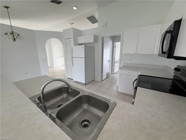 Kitchen featuring a double basin stainless steel sink with a high-arc faucet, white cabinetry, light countertops, and tile flooring