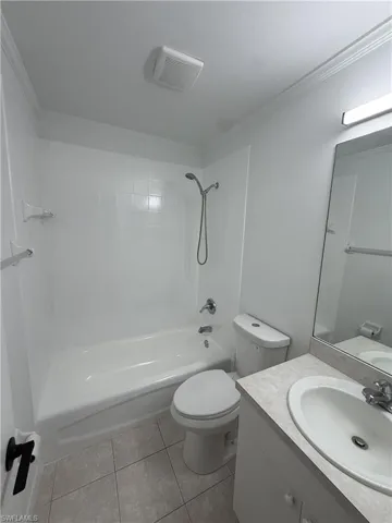 Bathroom featuring a white bathtub with a tiled shower surround, a white toilet, a white vanity with an integrated sink, a light-toned countertop, and a wall-mounted mirror