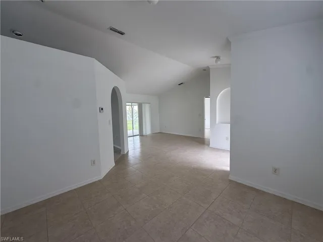 Spacious interior featuring vaulted ceilings, tile flooring, crown molding, arched doorways, and sliding glass doors