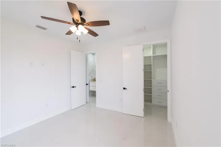 Unfurnished bedroom featuring a spacious closet, light marble finish floors, and a ceiling fan