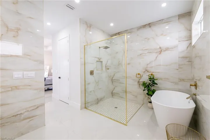Bathroom featuring stone wall, a marble finish shower, light marble finish floors, recessed lighting, and tile walls