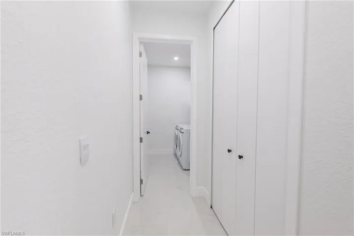 Corridor with a textured wall, washing machine and dryer, light marble finish flooring, and recessed lighting