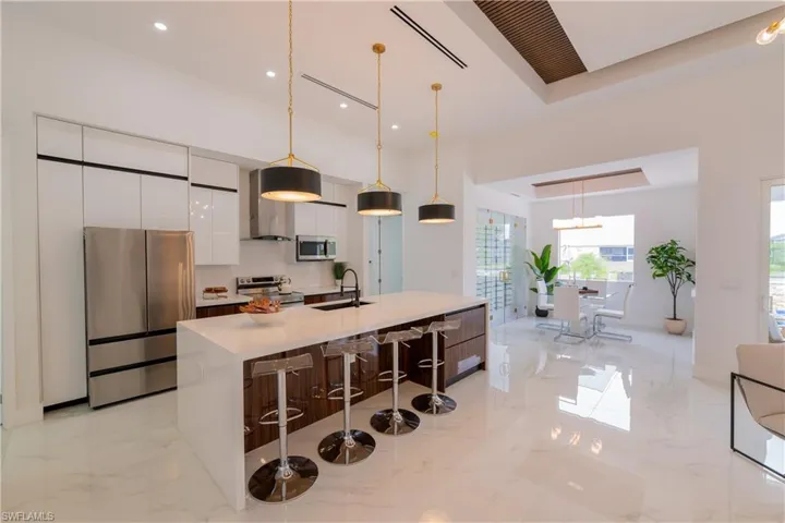 Two tone kitchen with stainless steel appliances, a kitchen island with sink, a breakfast bar area, ventilation hood, and decorative light fixtures