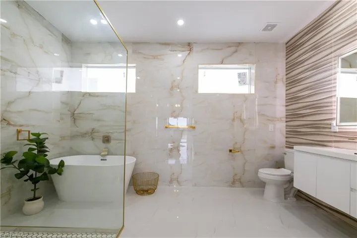 Bathroom with vanity, a freestanding bath, stone wall, and light marble finish flooring