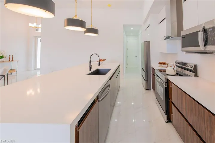 Dual tone kitchen with modern cabinets, stainless steel appliances, a large island with sink, decorative light fixtures, and light stone counters