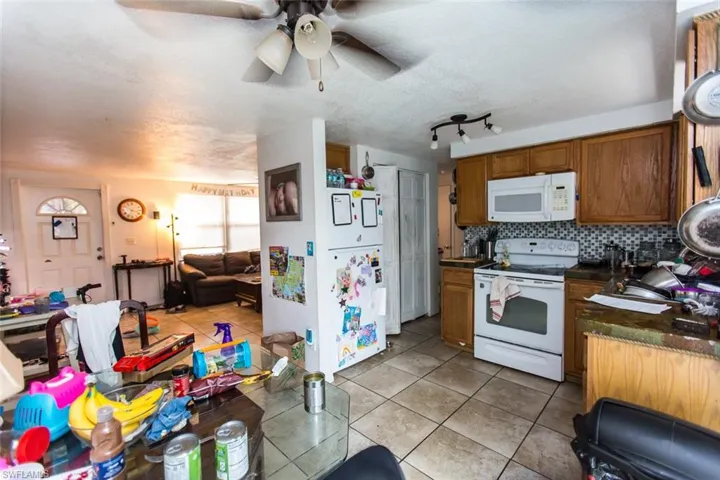 Kitchen featuring white appliances, backsplash, light tile patterned floors, rail lighting, and ceiling fan