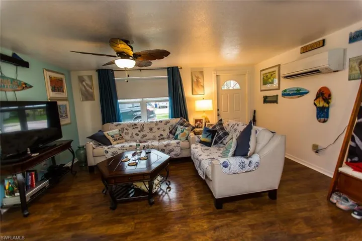 Living room with a wall unit AC, a textured ceiling, ceiling fan, and dark wood-type flooring