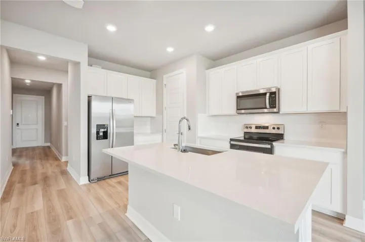 Kitchen featuring light hardwood / wood-style floors, sink, an island with sink, white cabinetry, and appliances with stainless steel finishes