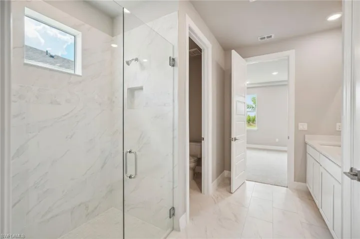 Bathroom featuring walk in shower, vanity, and toilet