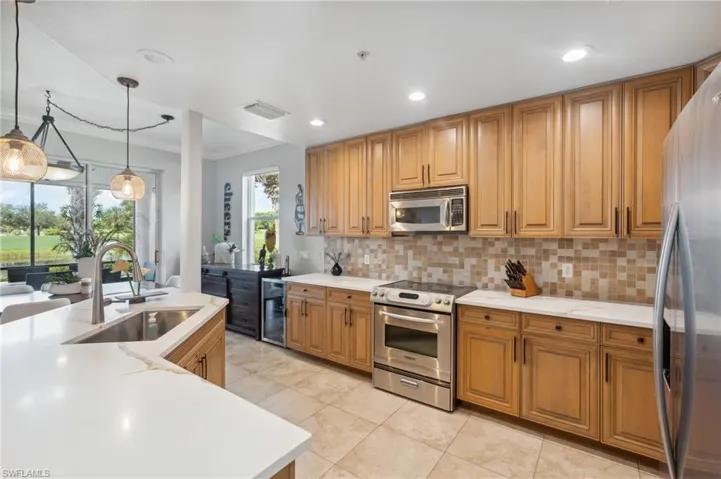 Kitchen with sink, beverage cooler, pendant lighting, appliances with stainless steel finishes, and ornamental molding