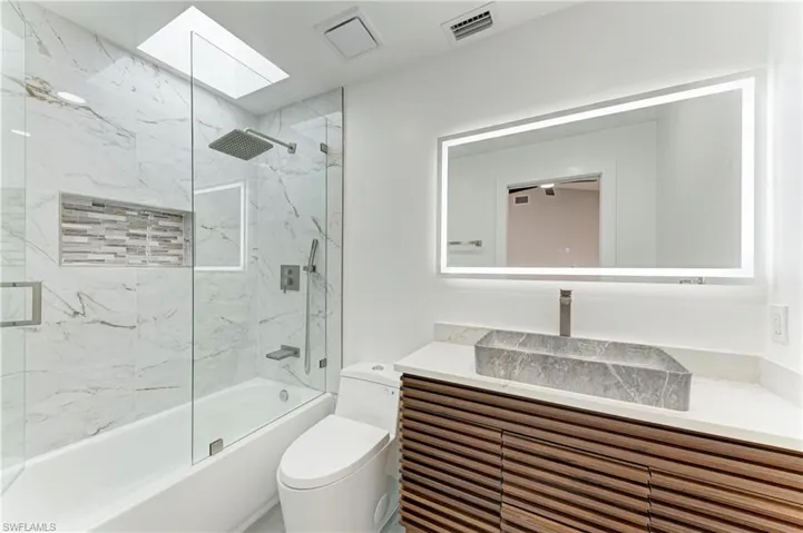 Bathroom featuring vanity, combined bath / shower with glass door, and a skylight