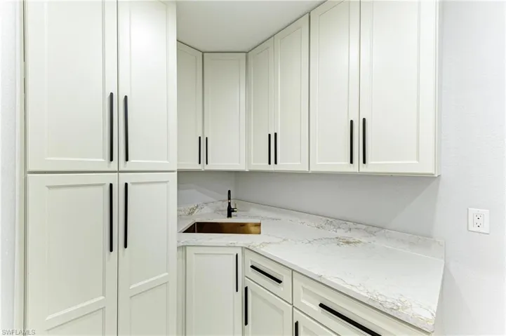 Bar featuring light stone countertops and white cabinetry