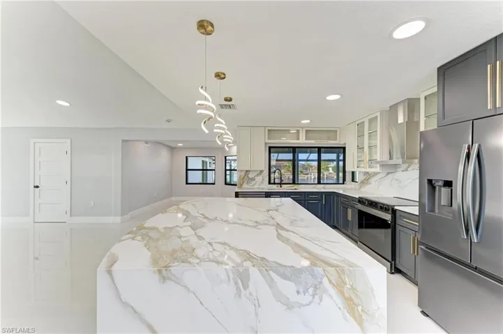 Kitchen featuring stainless steel appliances, light stone countertops, hanging light fixtures, glass insert cabinets, and wall chimney exhaust hood