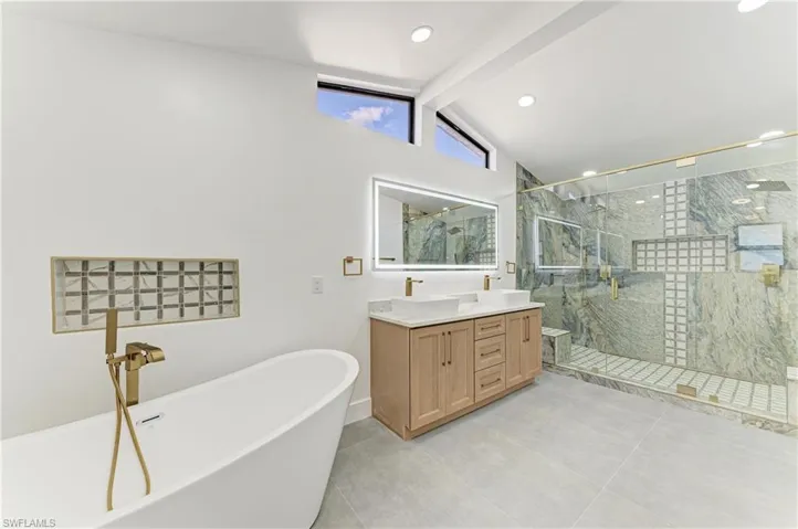 Full bathroom featuring a freestanding bath, double vanity, a marble finish shower, recessed lighting, and light tile patterned floors
