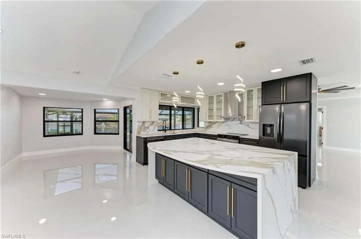 Kitchen featuring glass insert cabinets, a center island, stainless steel fridge with ice dispenser, light stone counters, and pendant lighting