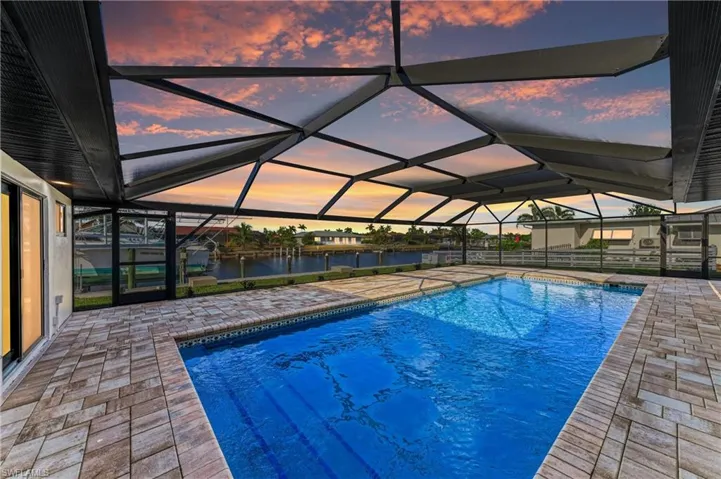 Pool at dusk with a sunroom, an outdoor pool, and a patio