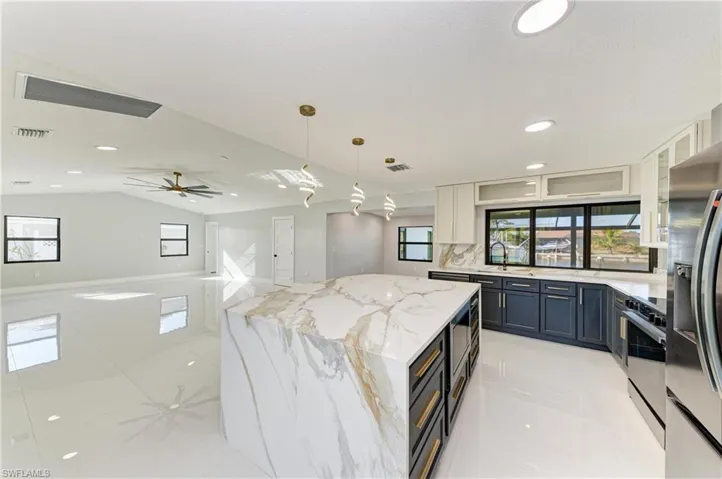 Kitchen featuring decorative light fixtures, light stone countertops, dark cabinets, stainless steel appliances, and recessed lighting