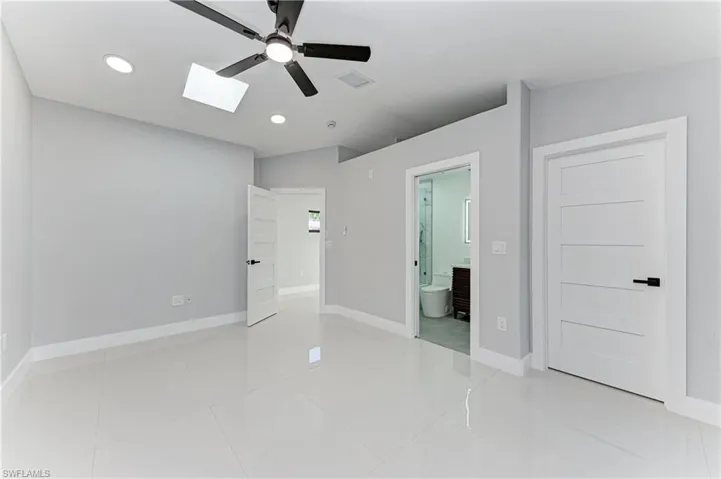 Unfurnished bedroom featuring a skylight, ceiling fan, connected bathroom, light tile patterned flooring, and recessed lighting