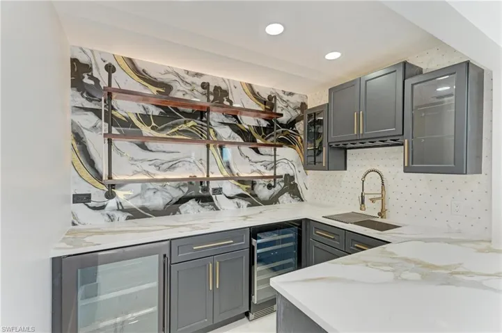 Bar featuring light stone countertops, wine cooler, gray cabinets, glass insert cabinets, and recessed lighting