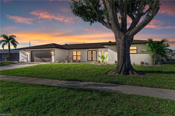 Mid-century home with a front yard, stucco siding, driveway, and a garage