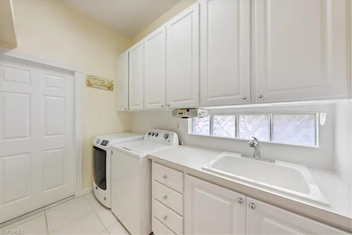 Clothes washing area featuring independent washer and dryer, cabinet space, a sink, and light tile patterned floors