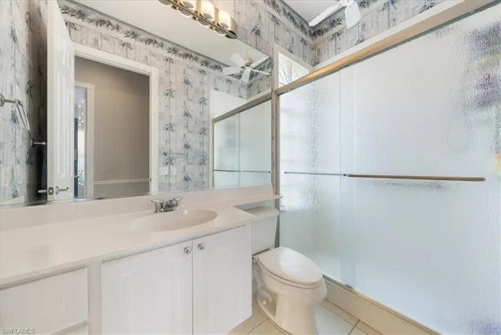 Full bath featuring wallpapered walls, tile patterned floors, toilet, vanity, and a stall shower