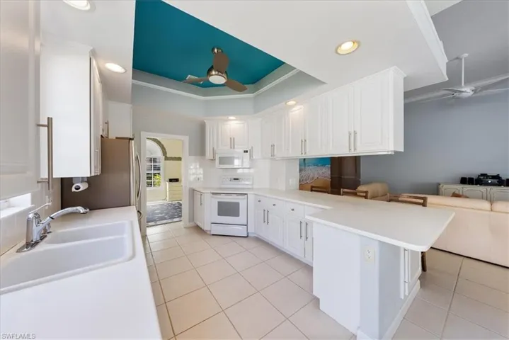Kitchen featuring a raised ceiling, a ceiling fan, white cabinetry, a peninsula, and white appliances