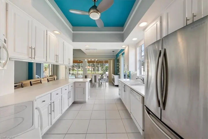 Kitchen with white cabinetry, light countertops, a tray ceiling, freestanding refrigerator, and white dishwasher