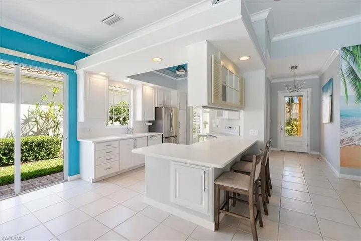 Kitchen with light countertops, ornamental molding, a sink, an inviting chandelier, and freestanding refrigerator