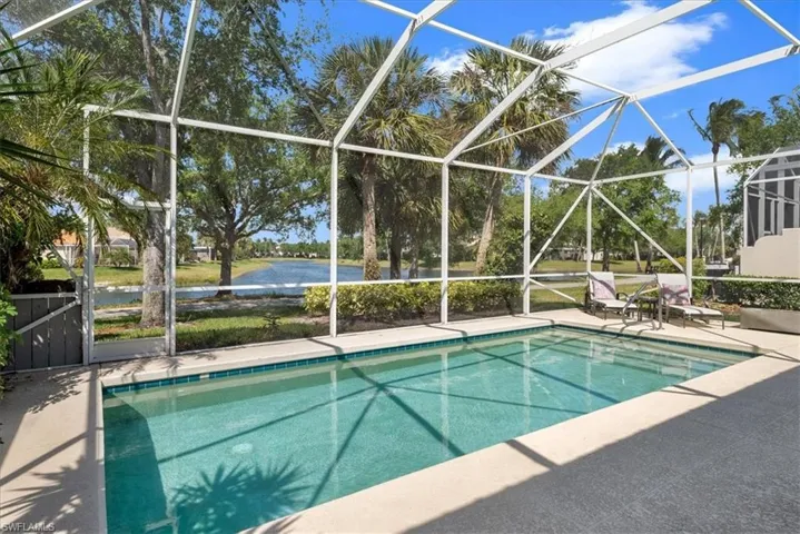 Outdoor pool with glass enclosure, a water view, and a patio area